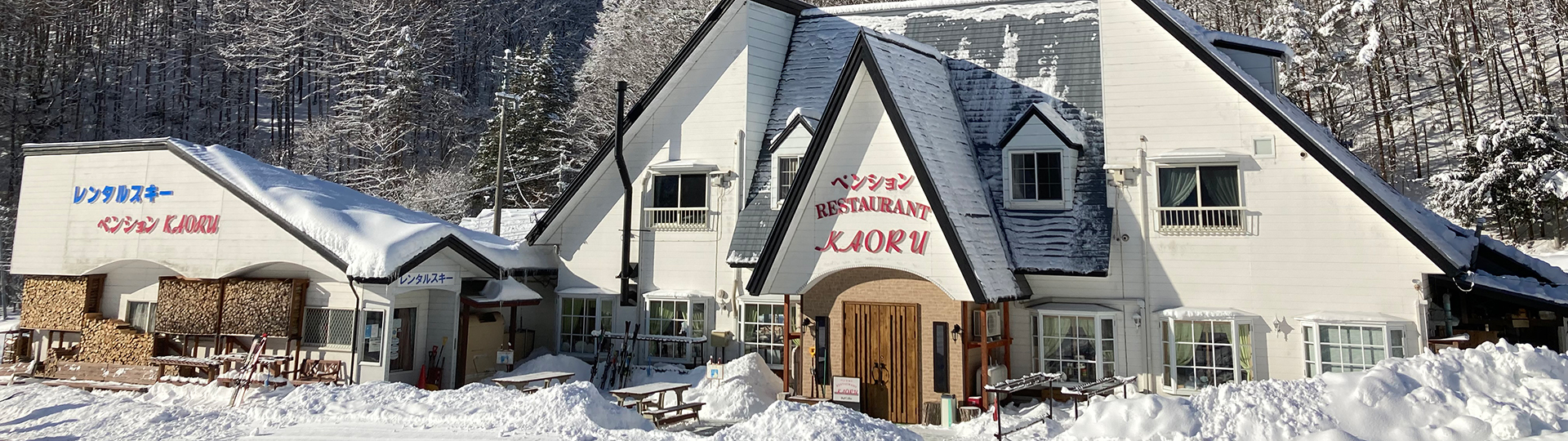 雪化粧した山を背に建つ、レンタルスキー ペンションKAORUの看板を掲げた建物