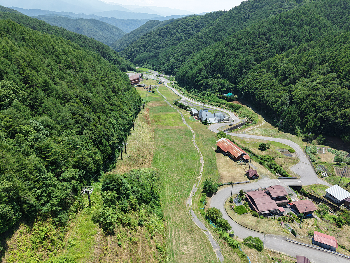 緑の山あいに広がる夏のスキー場ゲレンデを上空から