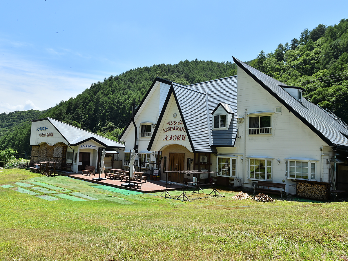 夏の青空と緑の山を背にしたペンションかおるの外観