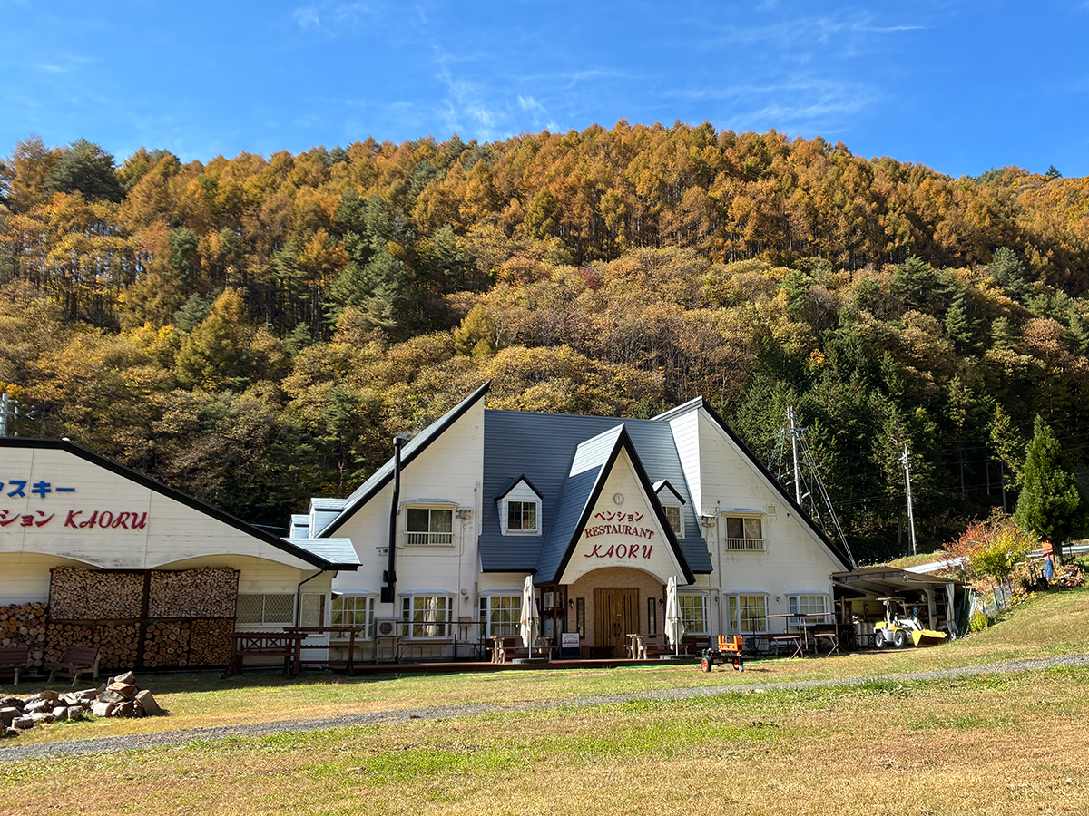色づいたカラマツの山を背にしたペンションかおるの外観